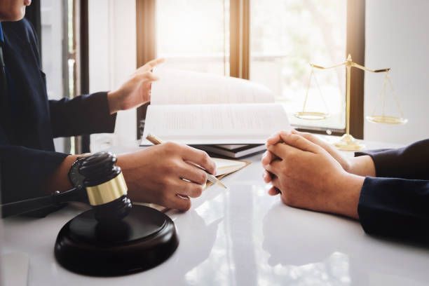 Lawyer meeting with client at desk with legal documents, gavel, and scales of justice.