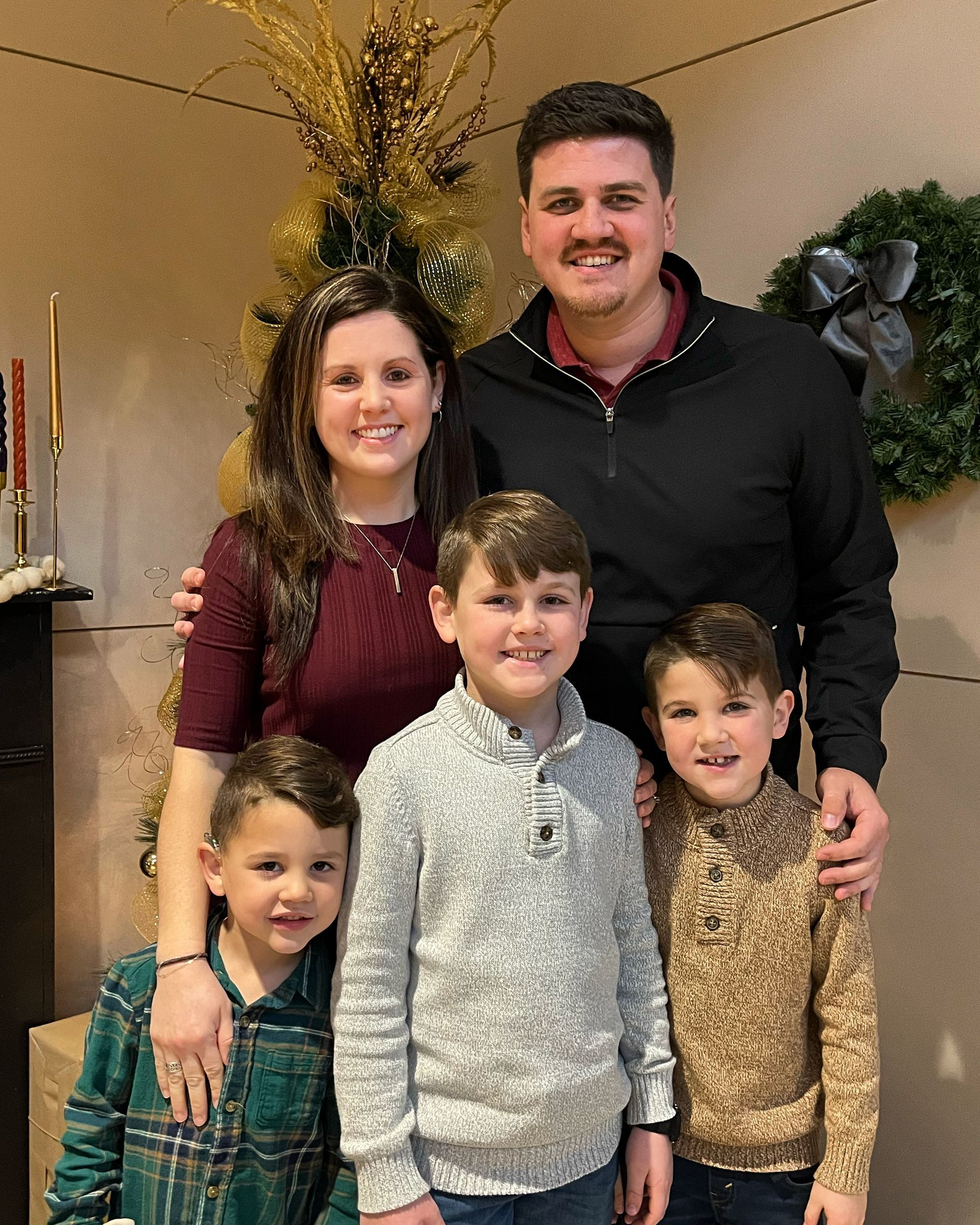 Family of five posing together; woman, man, and three young boys in front of a decorated wall.