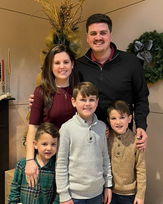 Family of five posing together in front of festive decorations; smiles, embracing.