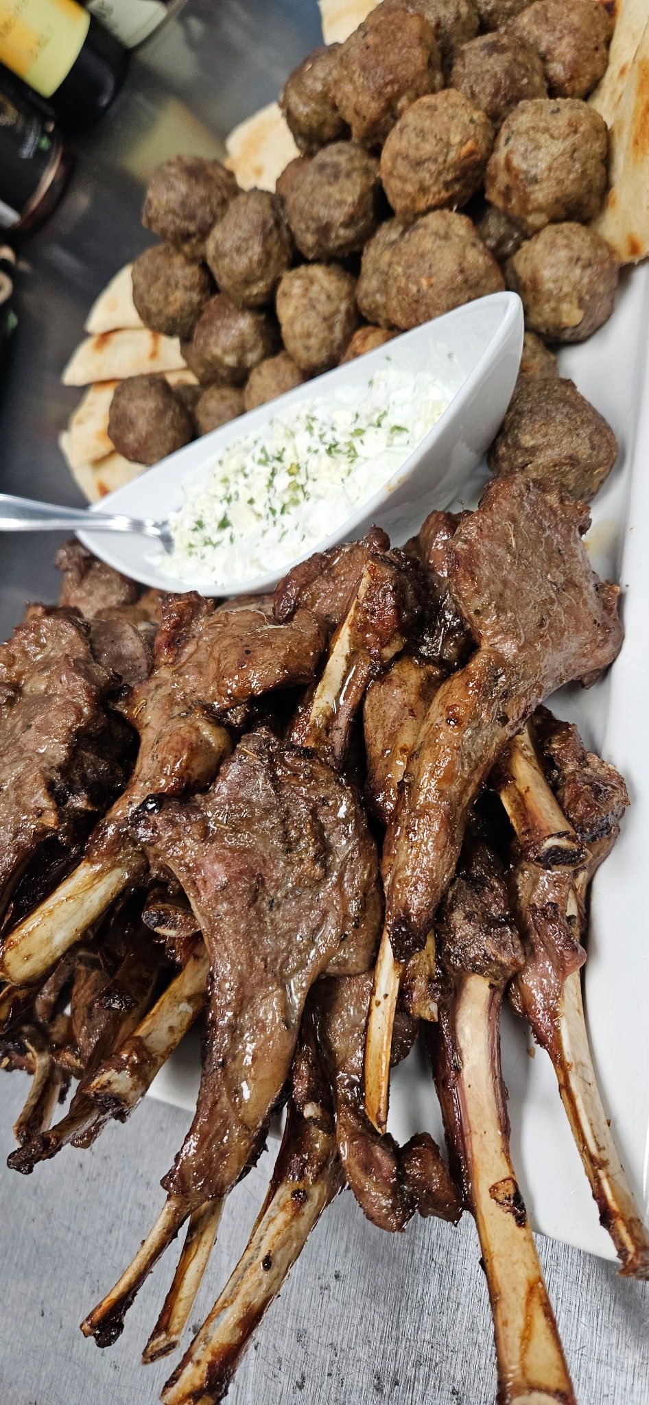 Lamb chops, meatballs, and tzatziki dip on a white platter.