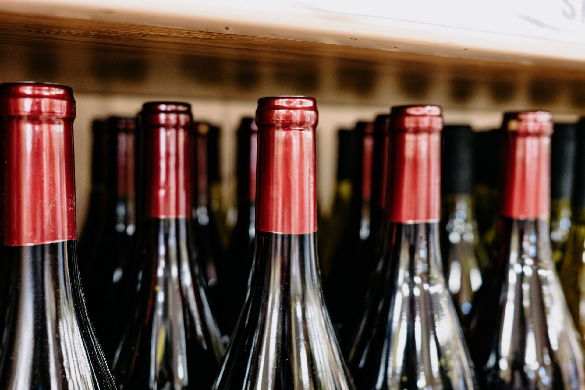 A row of wine bottles with red caps are lined up on a shelf.