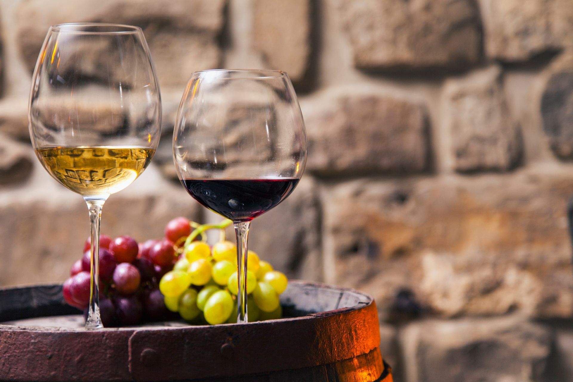 Two glasses of wine and grapes on a wooden barrel.