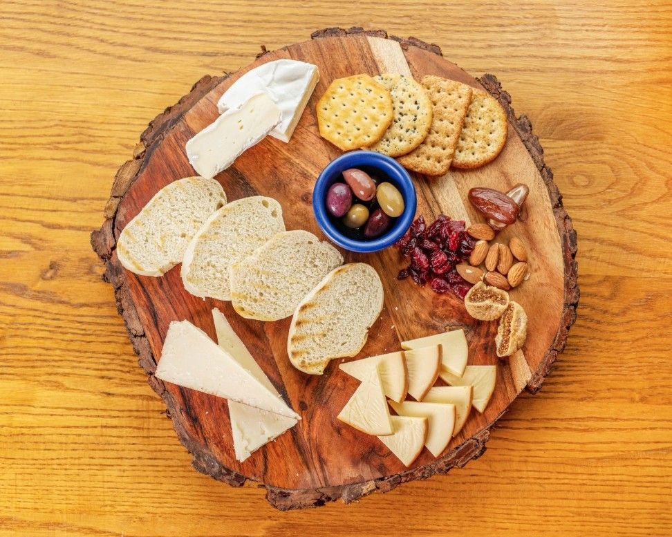 Wooden charcuterie board with assorted cheeses, crackers, nuts, olives, and grapes on a table