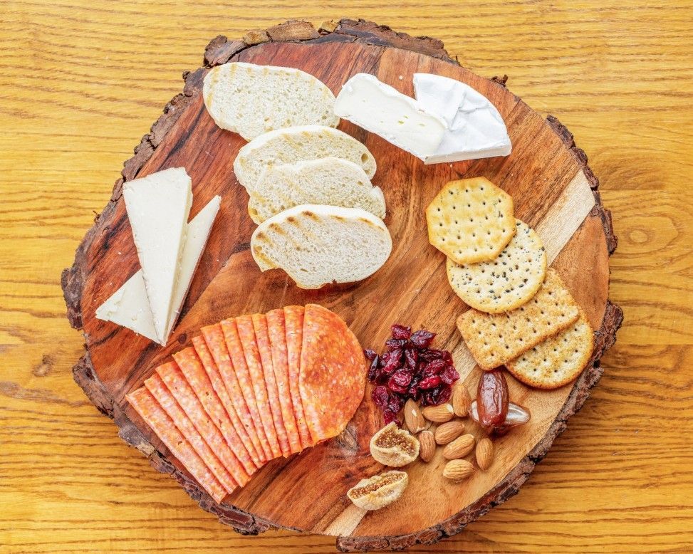 Cheese and crackers arranged on a round wooden board with nuts and dried fruit on a wood table