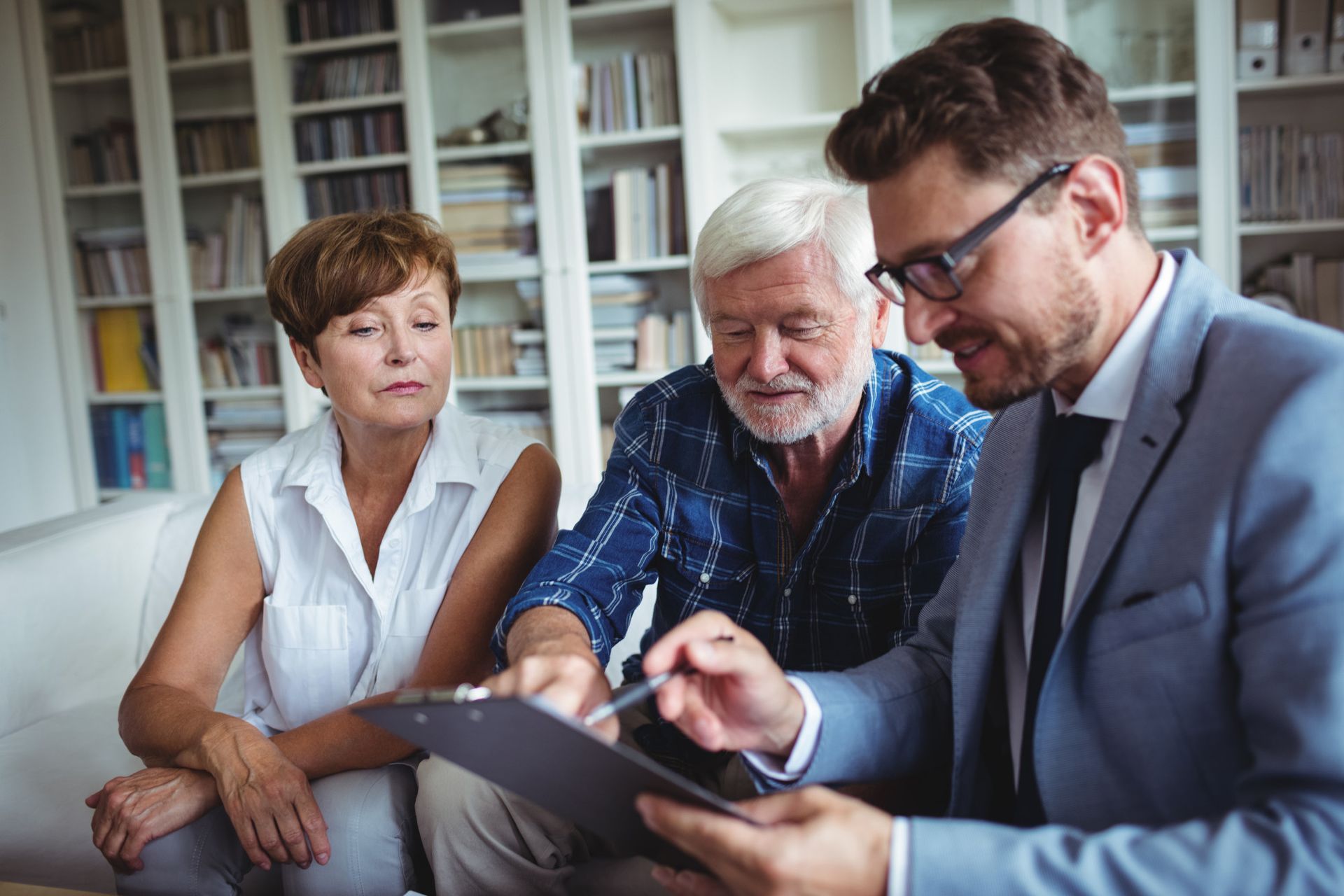 A financial advisor showing documents to an elderly couple in a home office setting.