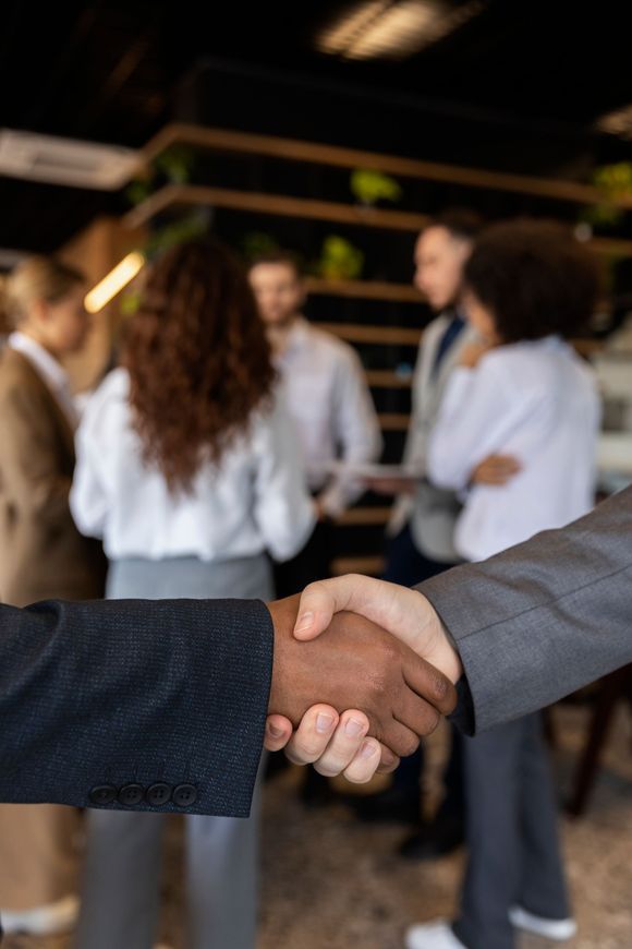 Two people shake hands in front of a group of people in an office setting.