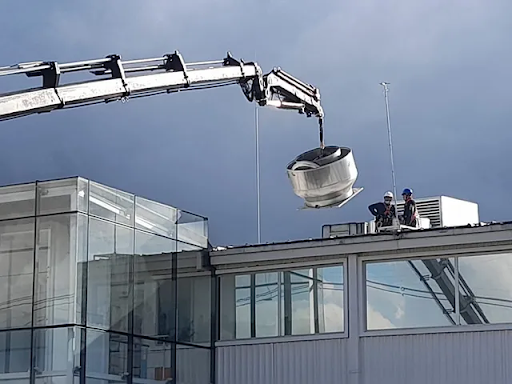 Una grúa está levantando un objeto grande en la parte superior de un edificio.