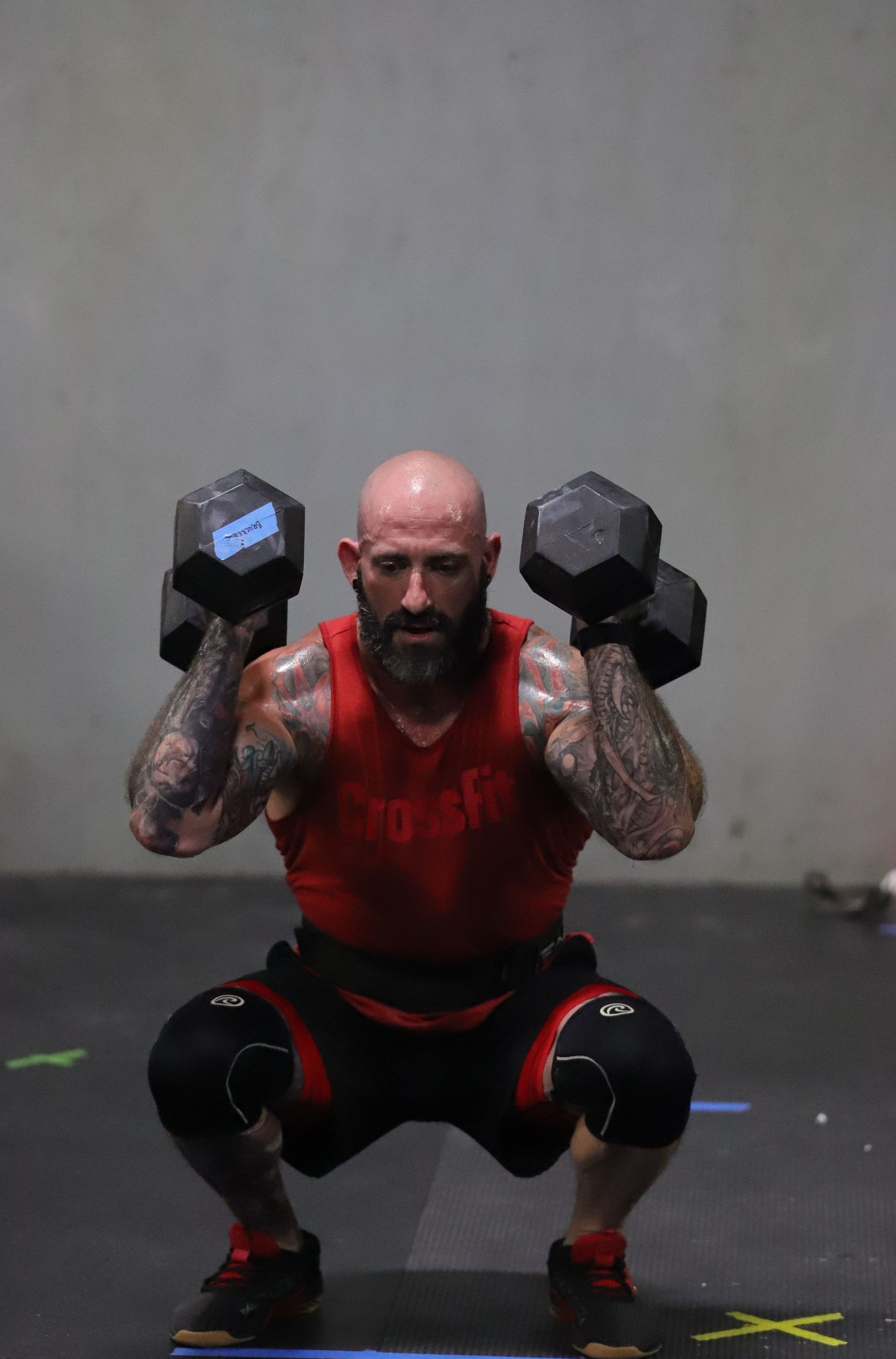 A man hoists two dumbbells on his shoulders.