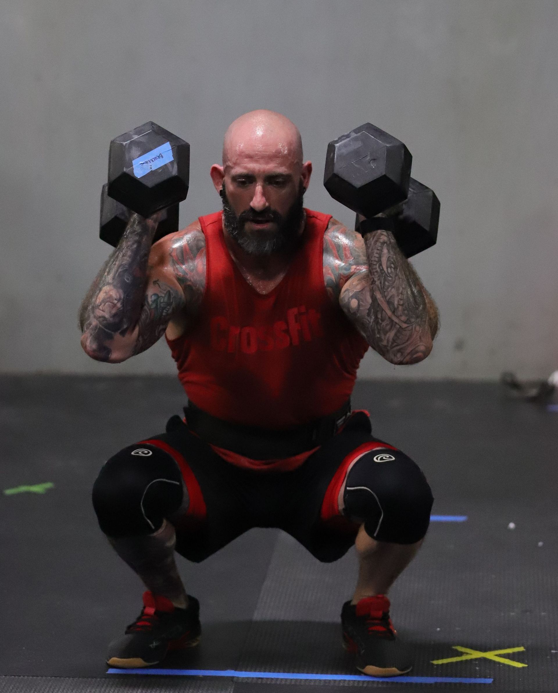 A man hoists two dumbbells on his shoulders.