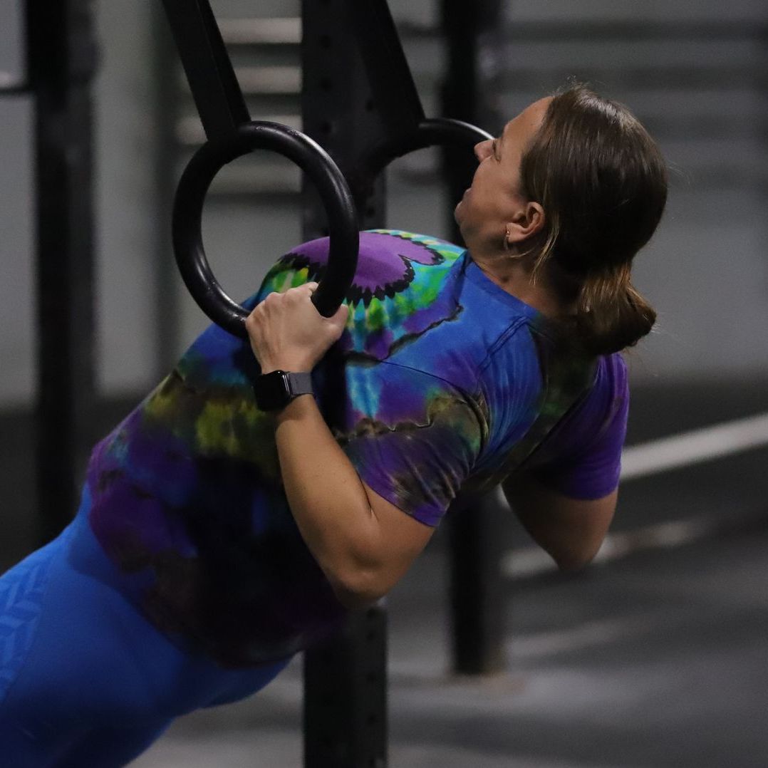 A woman wearing a tie-die shirt performing a ring-row.