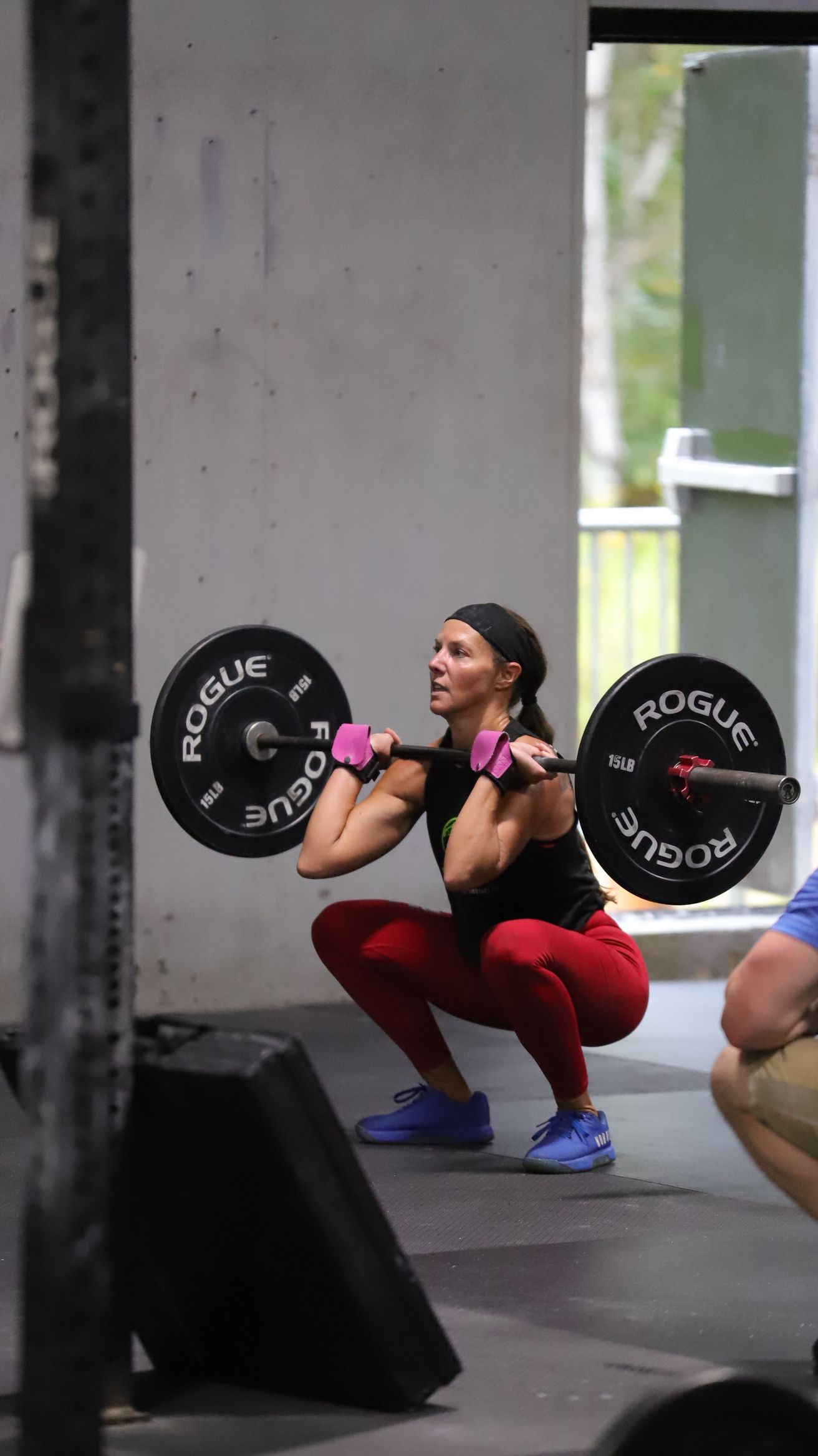 A woman in red pants and a black shirt lifts a barbell.