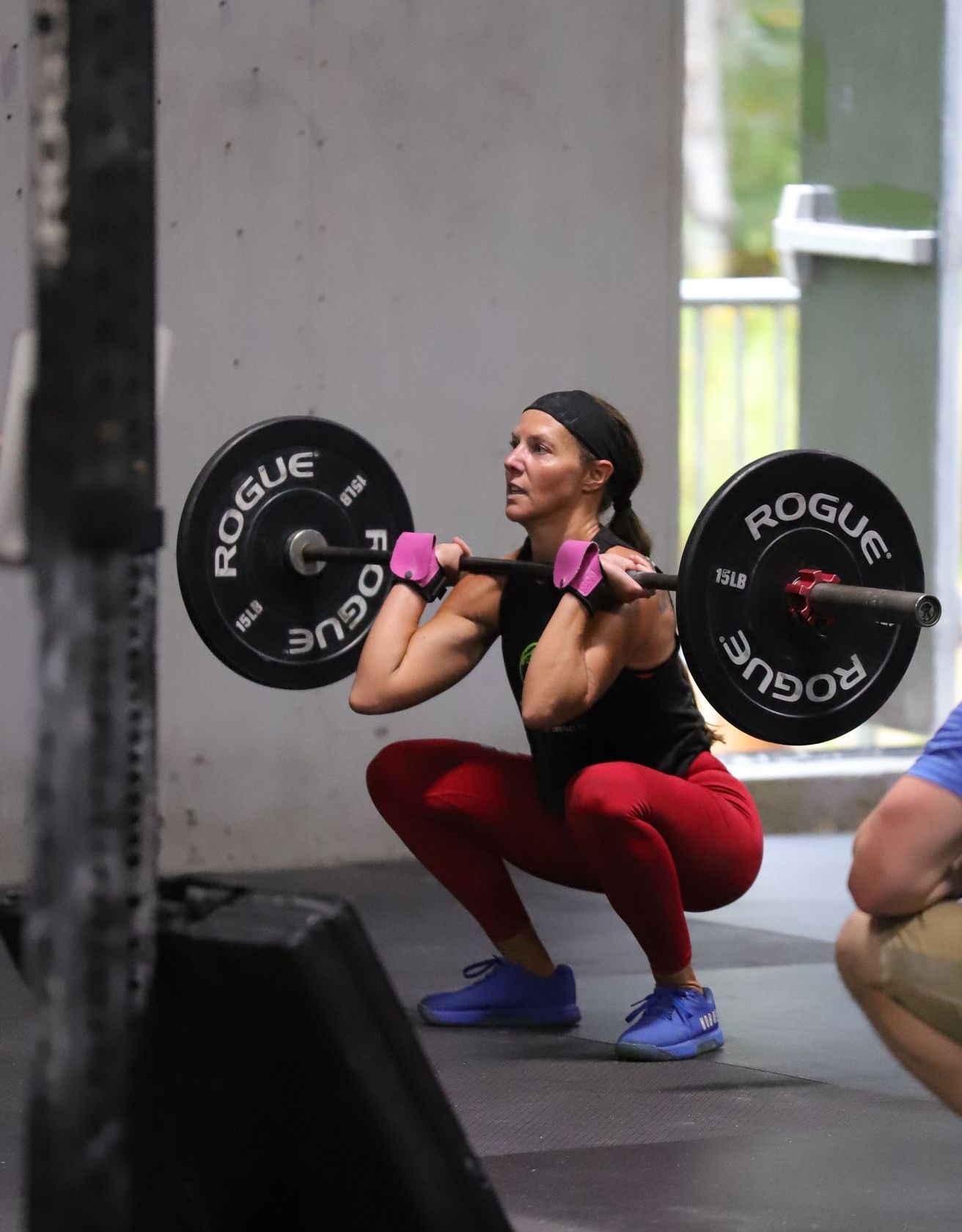 A woman in red pants and a black shirt lifts a barbell.