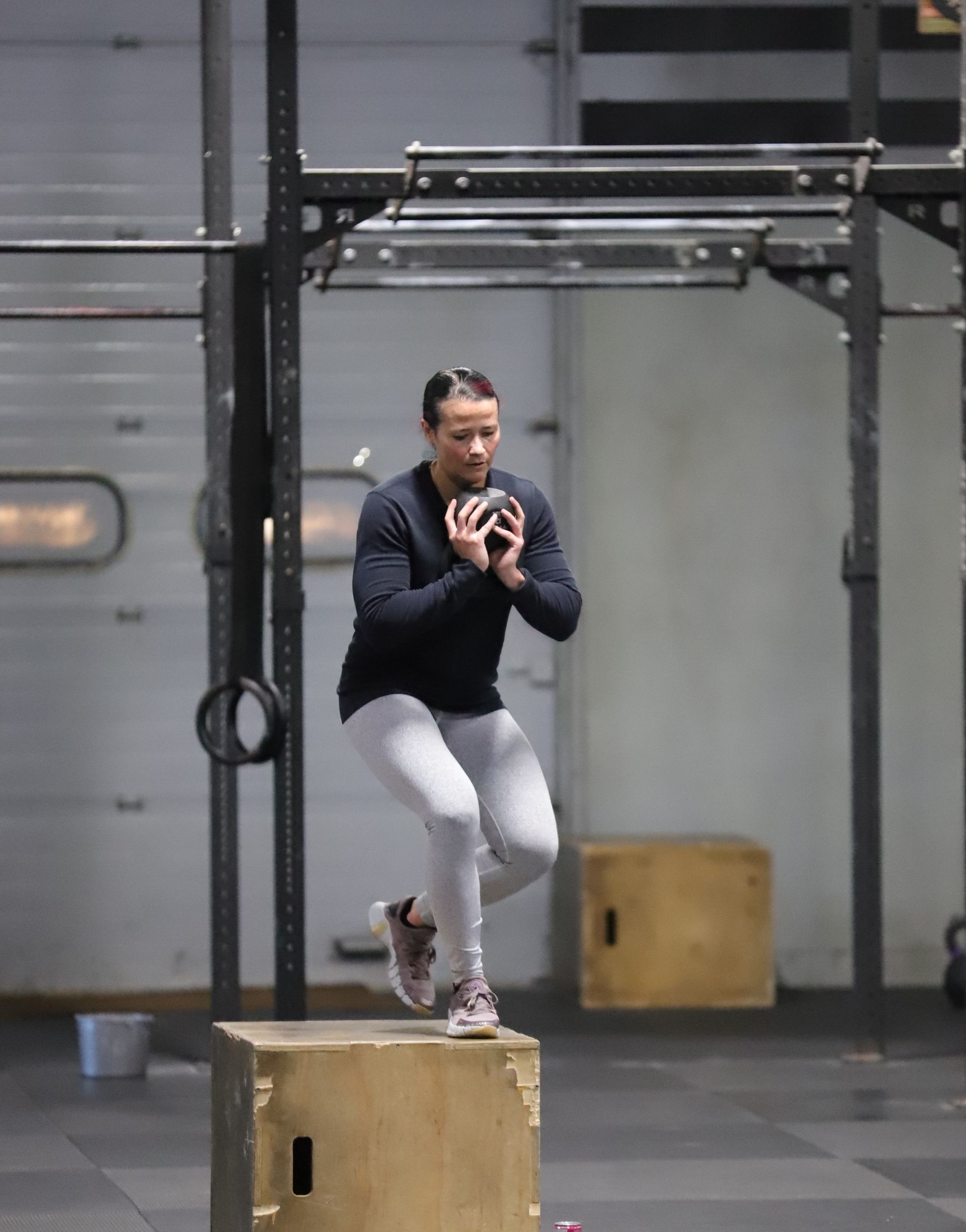 A woman steps down from a box while holding a kettle bell.