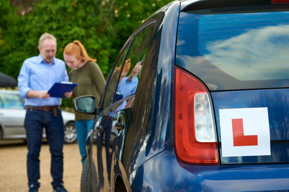 A Man and a Woman Are Standing Next to a Blue Car — NT Driving Academy in Casuarina, NT