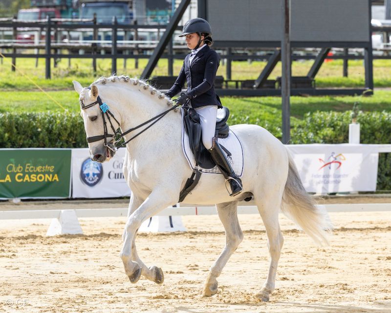 A woman is riding a white horse on a dirt track.