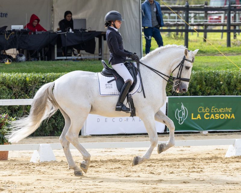 A woman is riding a white horse in front of a club equestre la casona sign