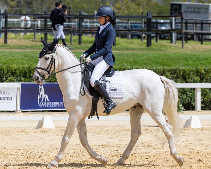A woman is riding a white horse on a dirt track.