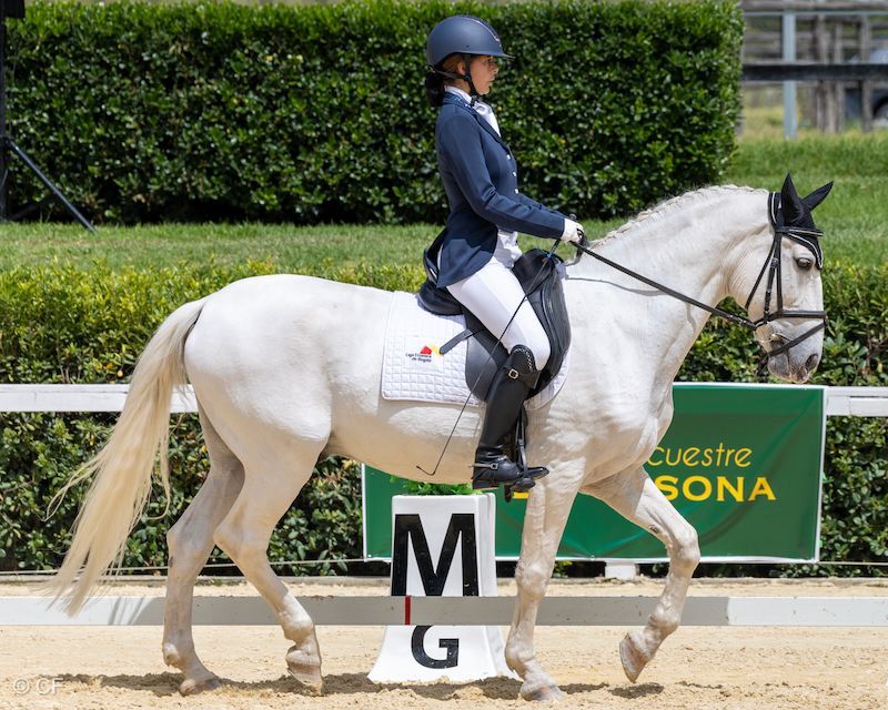 A woman is riding a white horse in front of a sign that says sona