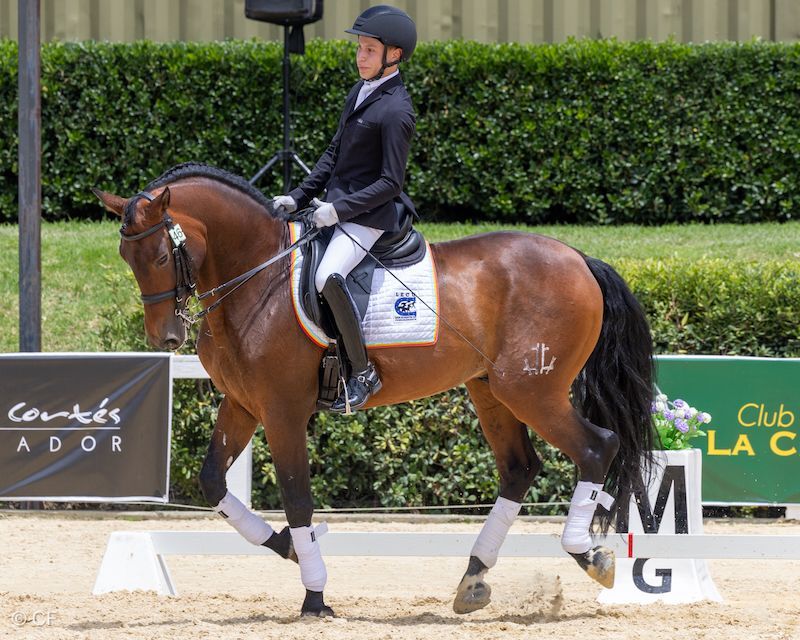 A man is riding a brown horse in front of a sign that says club la c