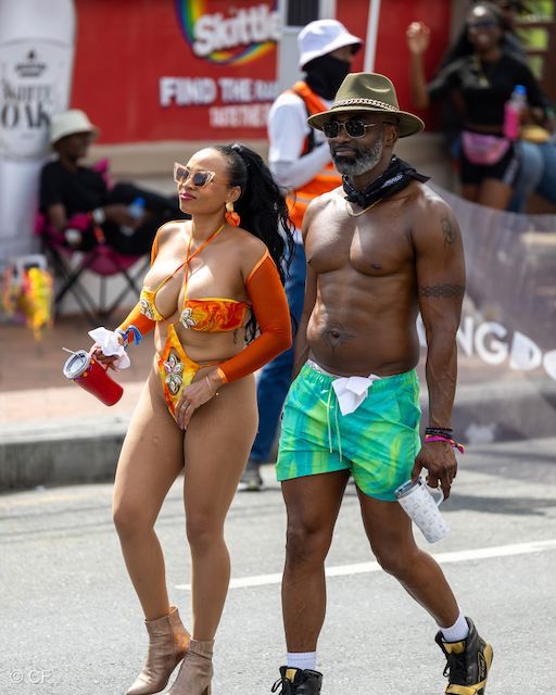 A man and a woman are walking down the street in front of an advertisement for skittles