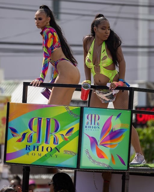 Two women in bikinis are standing on top of a sign that says ar rhion company
