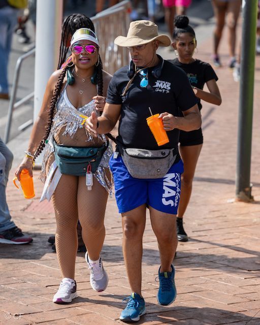 A man wearing blue shorts that say mas is walking with a woman