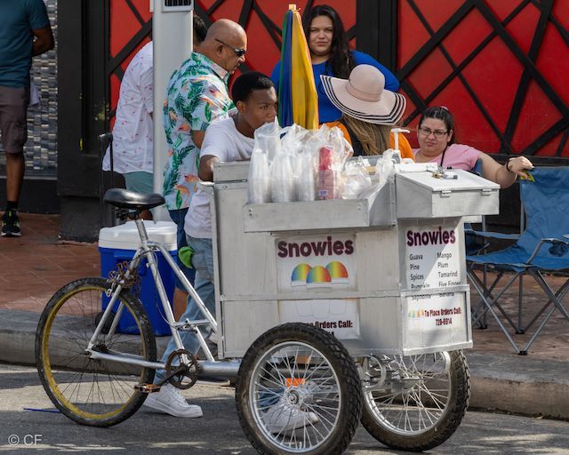 A group of people standing around a cart that says snowies on it