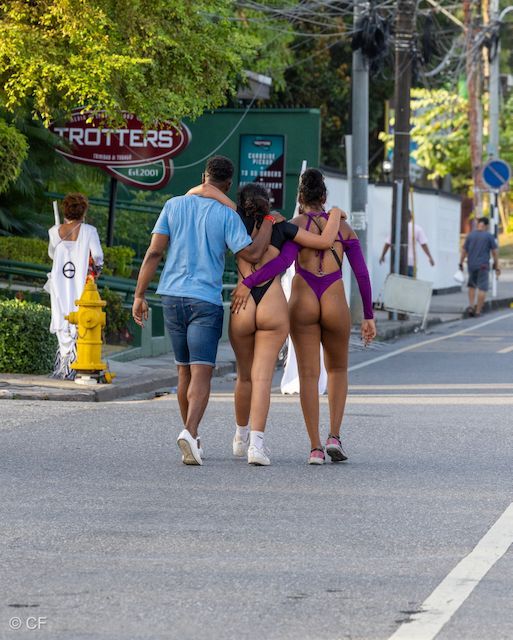 A man and two women are walking down a street in front of a sign that says trotters