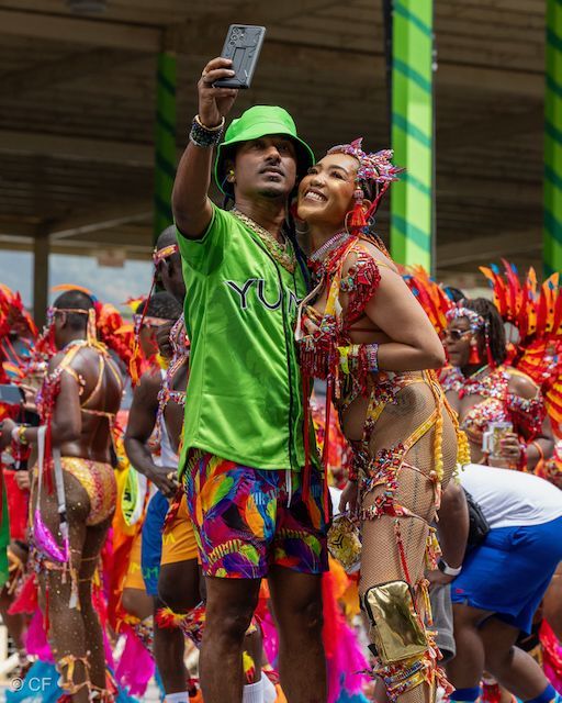 A man in a green shirt is taking a selfie with a woman in a colorful outfit.