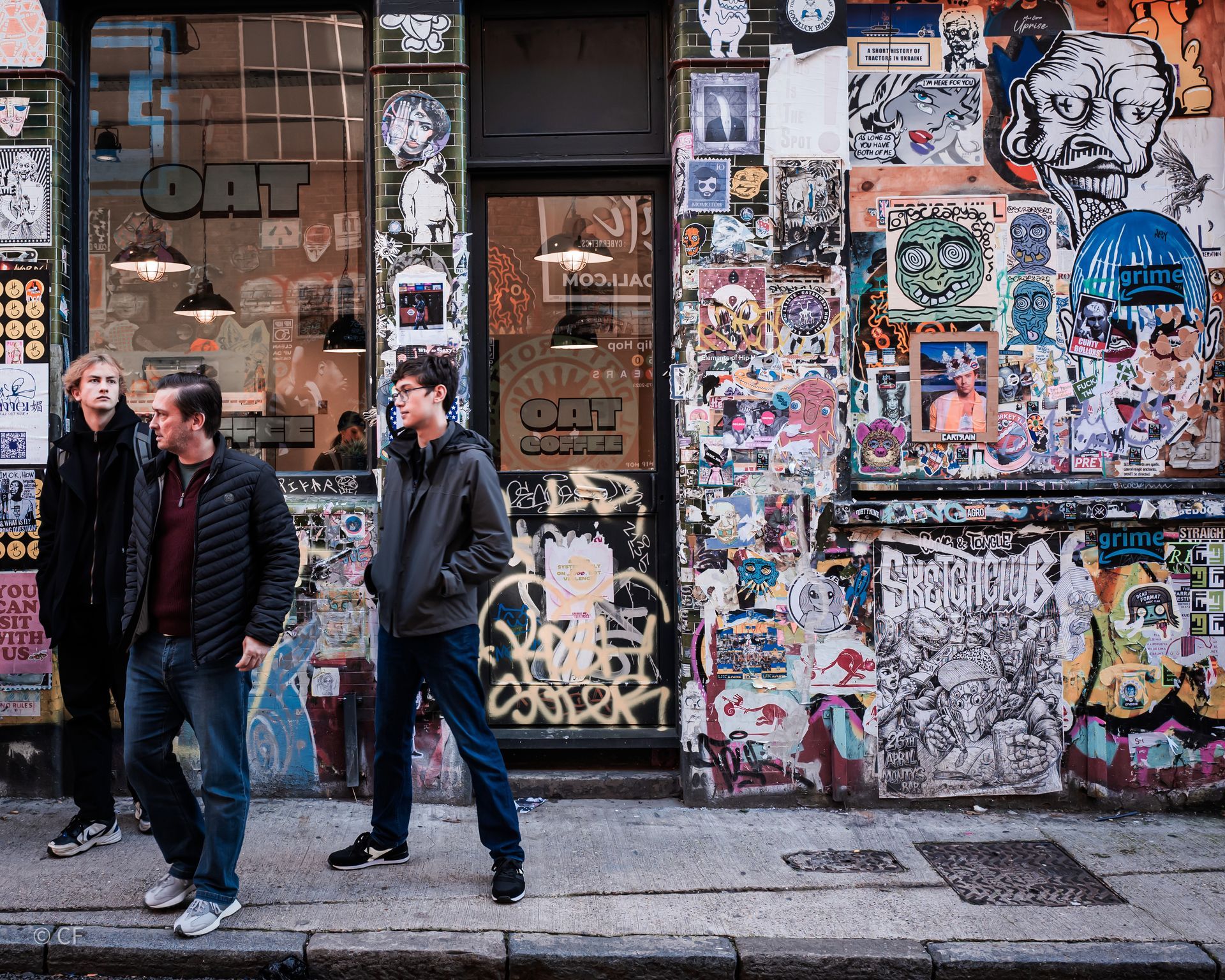 Three men are walking down a street in front of a building with graffiti on it.