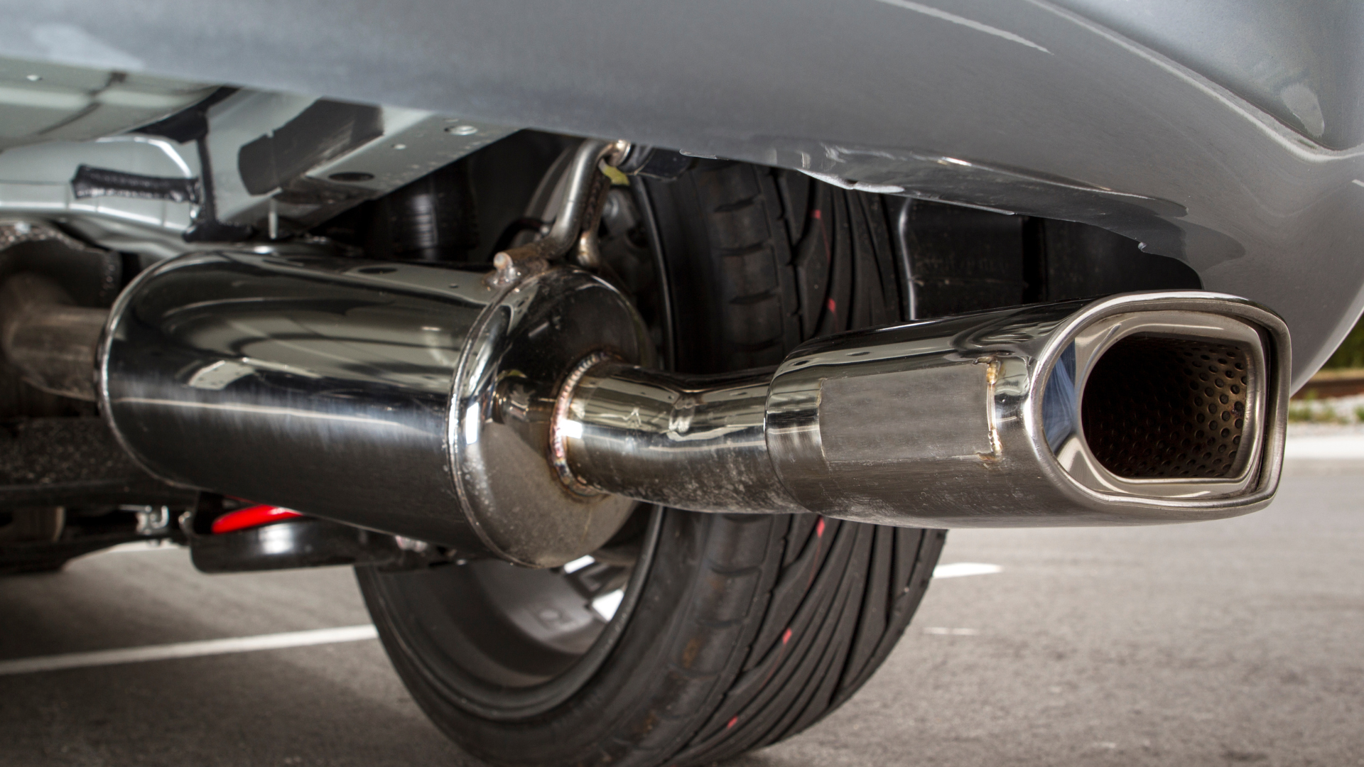 A car with a stainless steel exhaust pipe is parked on the side of the road.