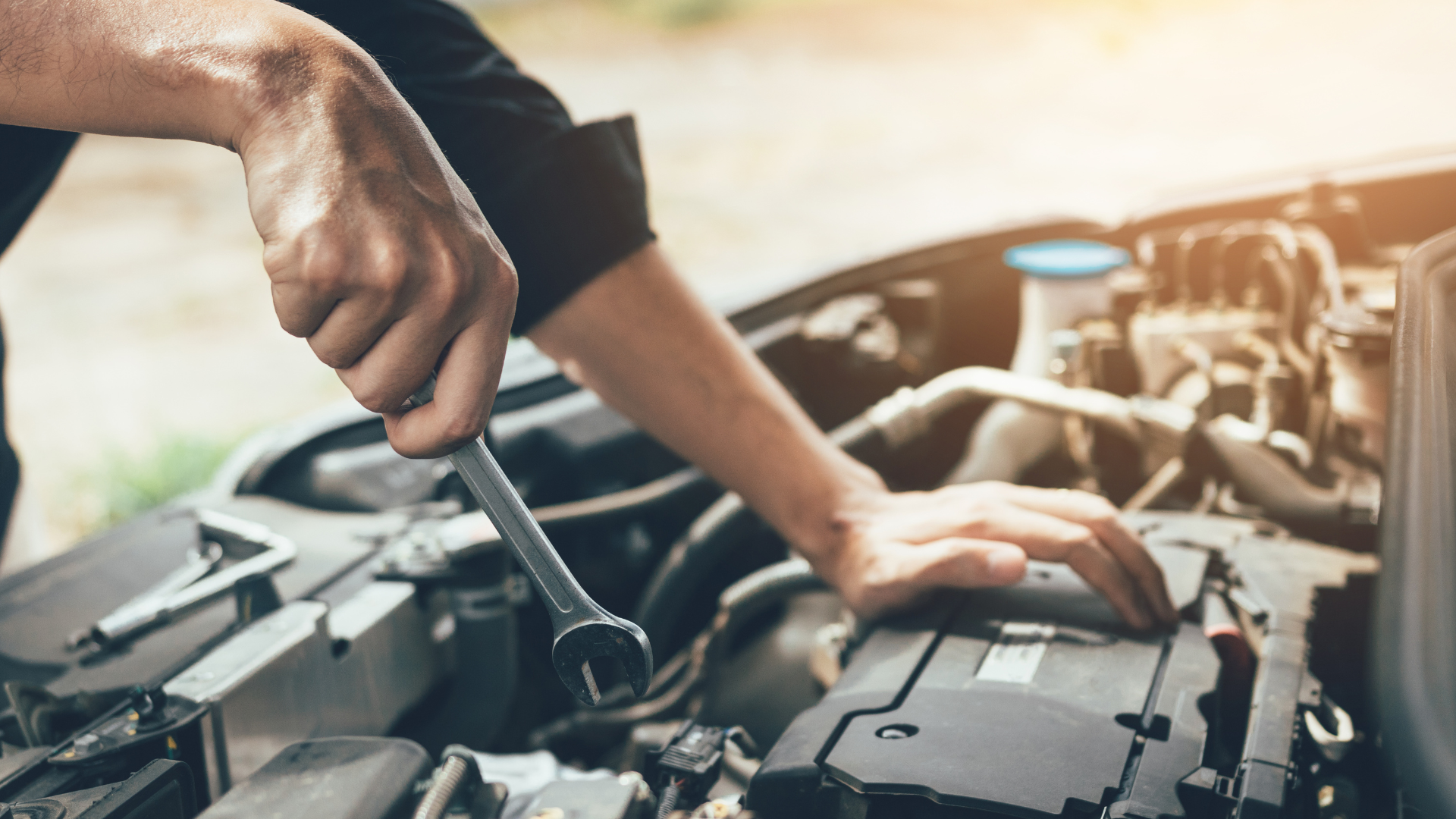 A man is working on the engine of a car with a wrench.