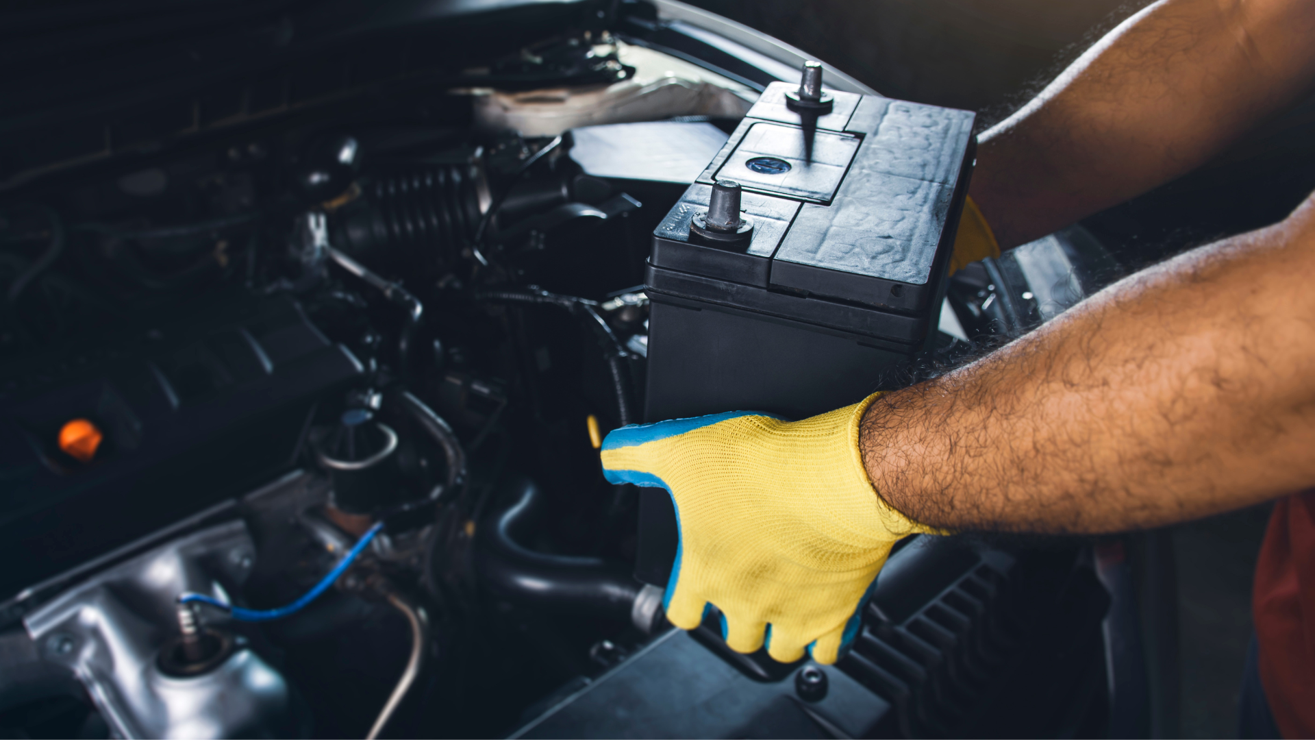 A man wearing yellow gloves is working on a car battery.