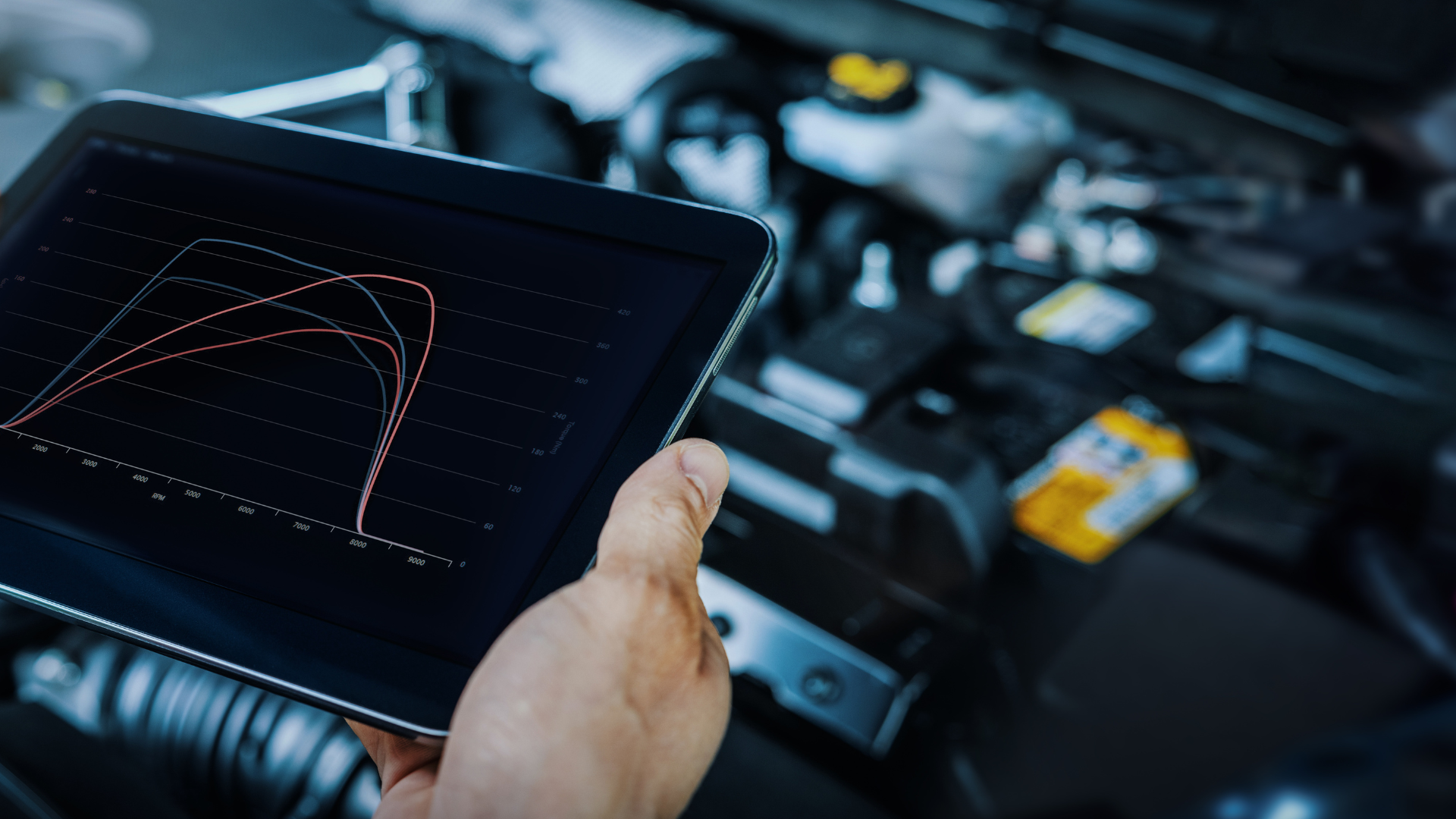 A person is holding a tablet in front of a car engine.