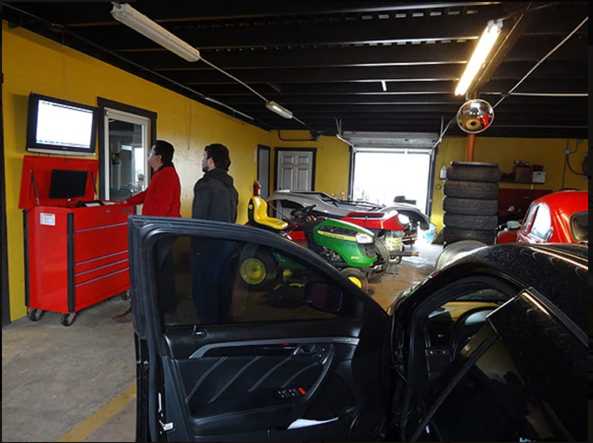 Two men are standing in a garage talking to each other