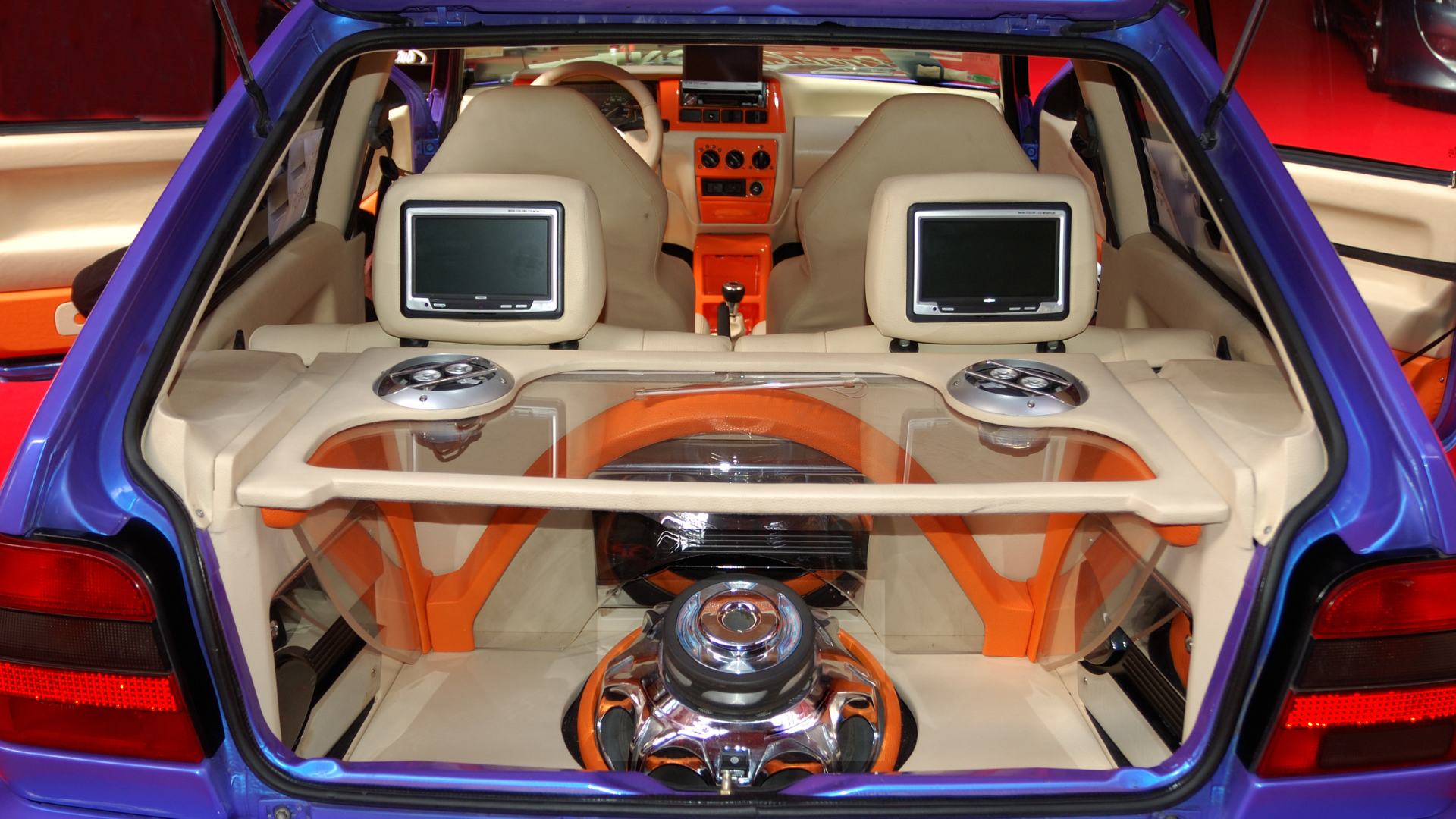 The trunk of a purple car with a stereo and two monitors