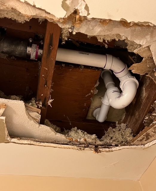 Damaged ceiling with exposed white PVC drain pipes and wooden supports. Insulation visible.