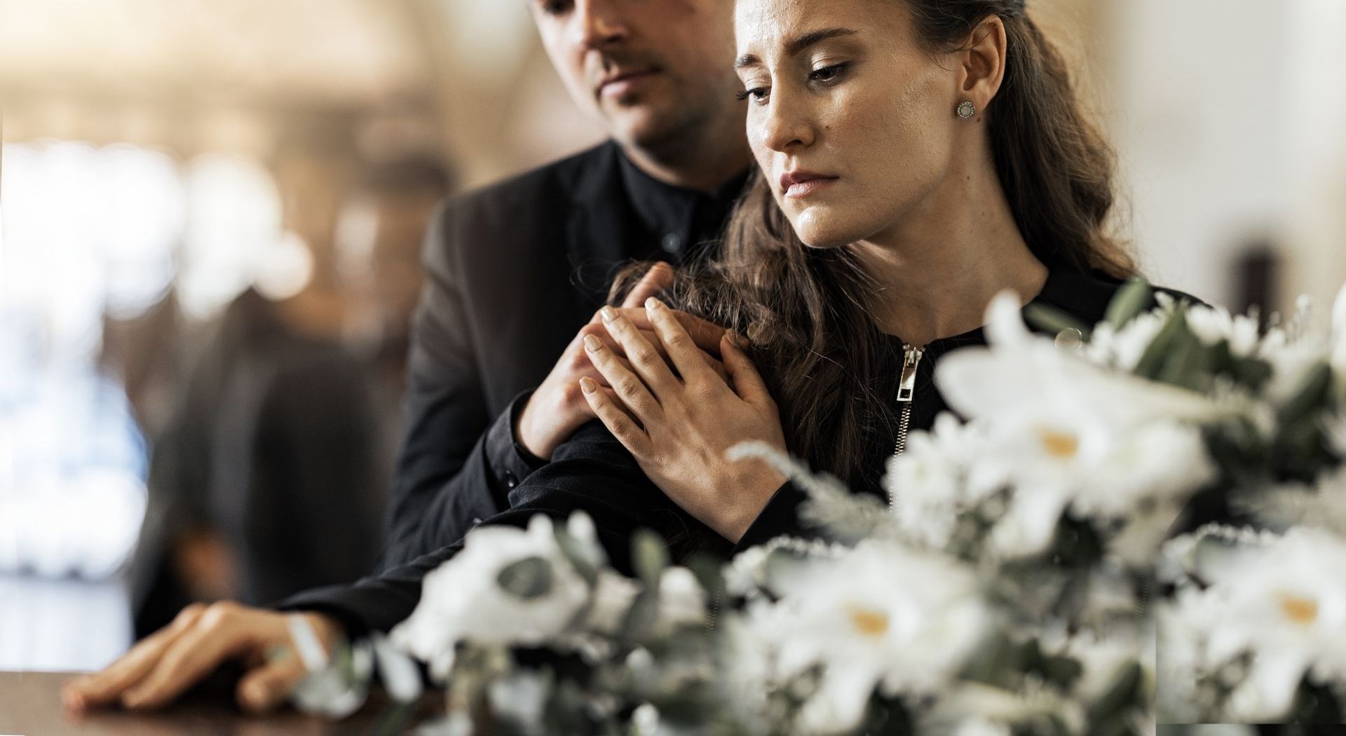 A man and a woman are standing next to a coffin at a funeral.