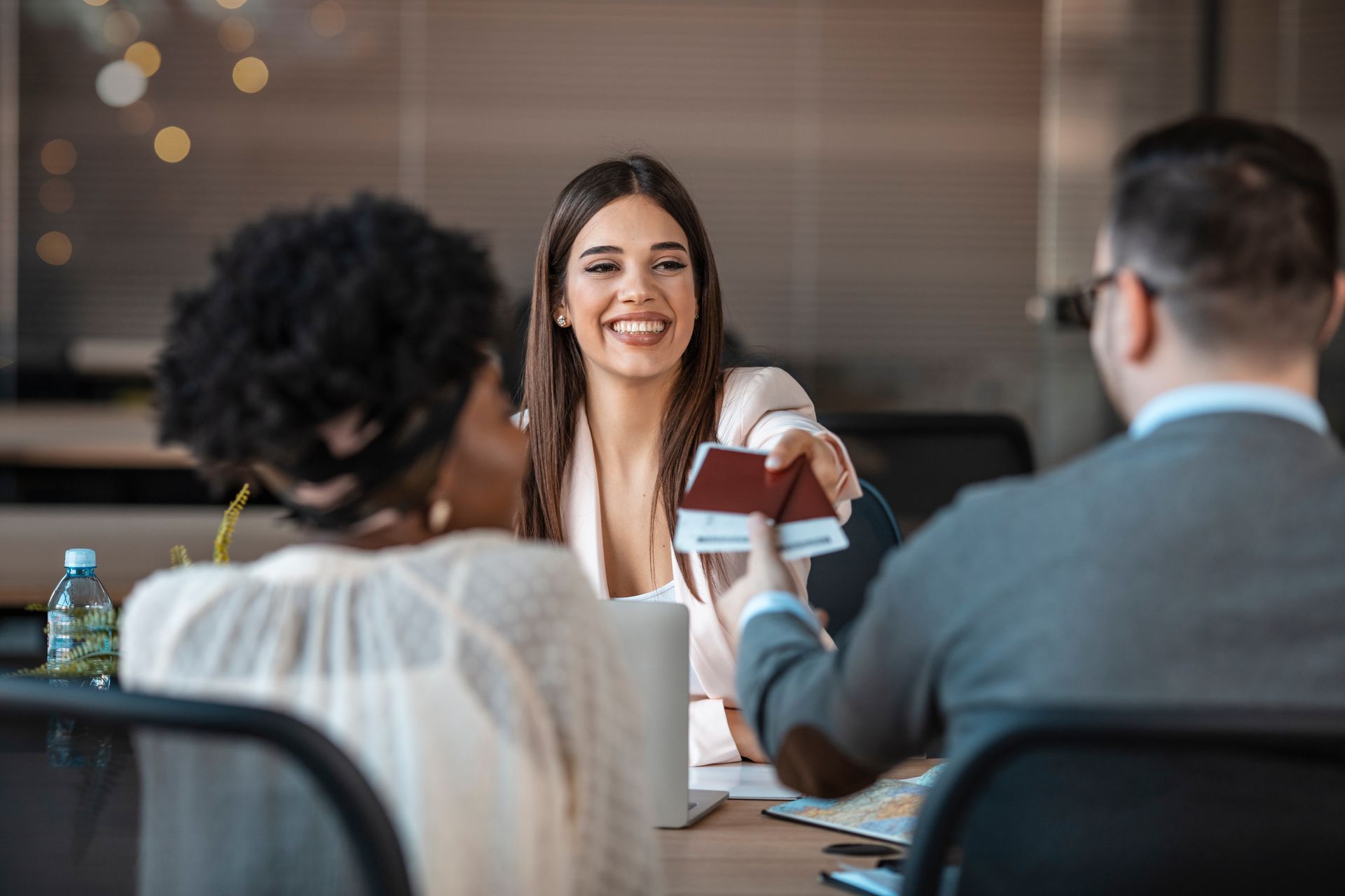 A woman is giving a passport to a man and a woman while sitting at a table.