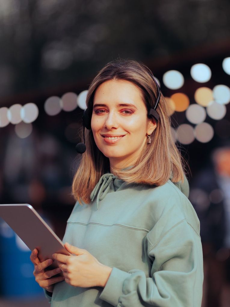 A woman wearing headphones is holding a tablet and smiling.