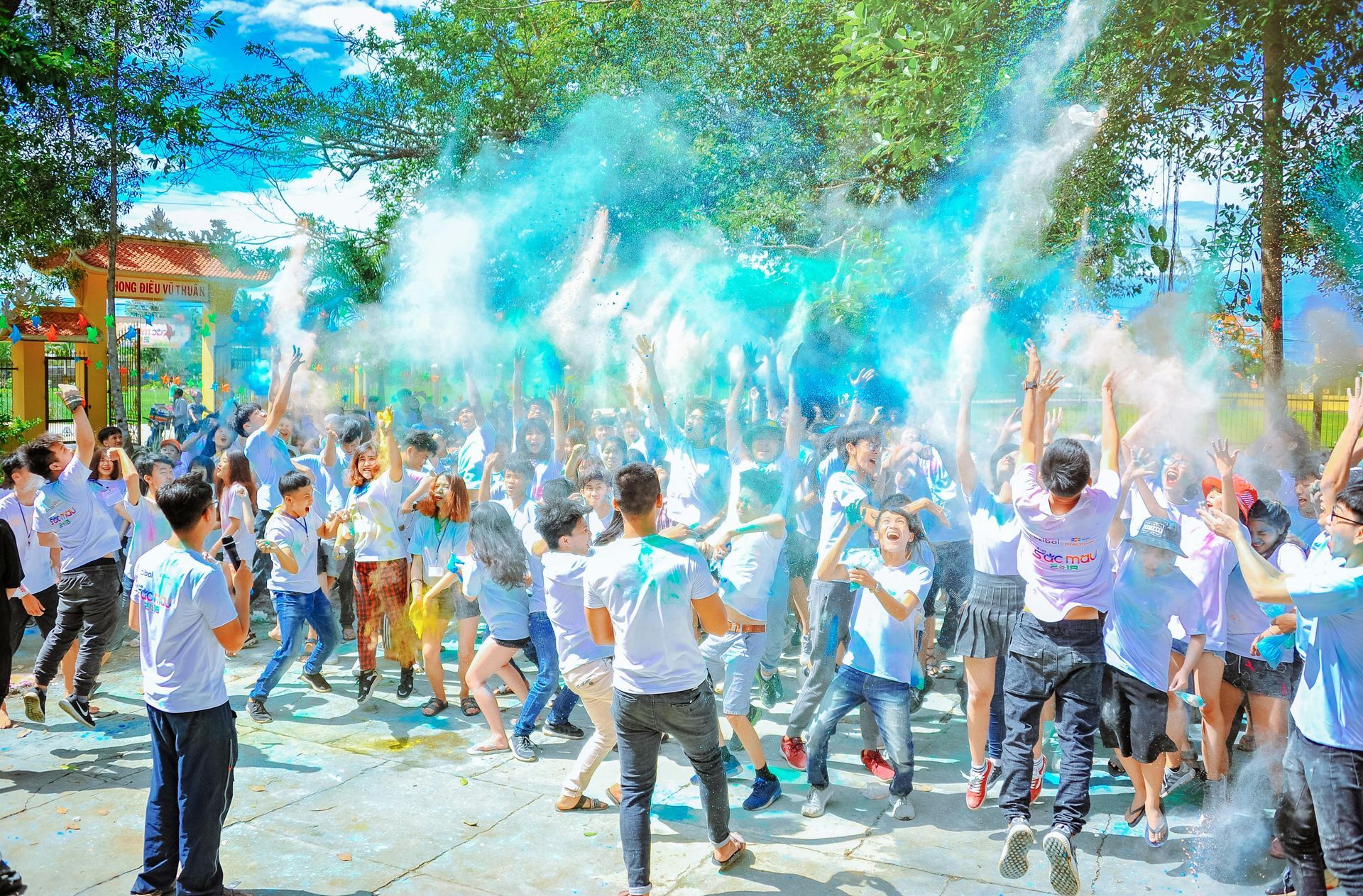 A large group of people are dancing and throwing blue powder in the air.