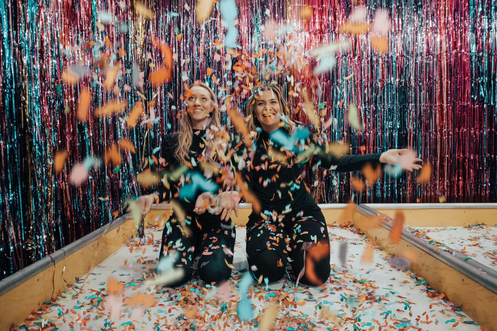 Two women are kneeling in a pool of confetti.