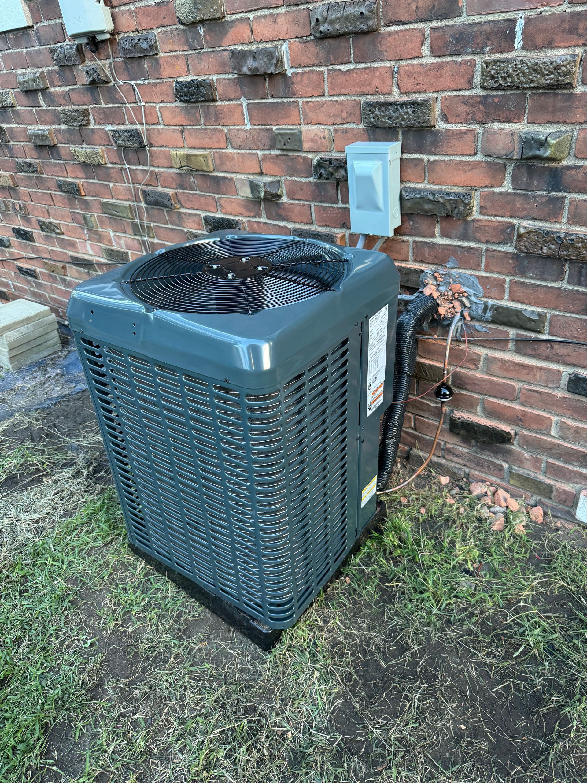 A gray air conditioner is sitting next to a brick wall.