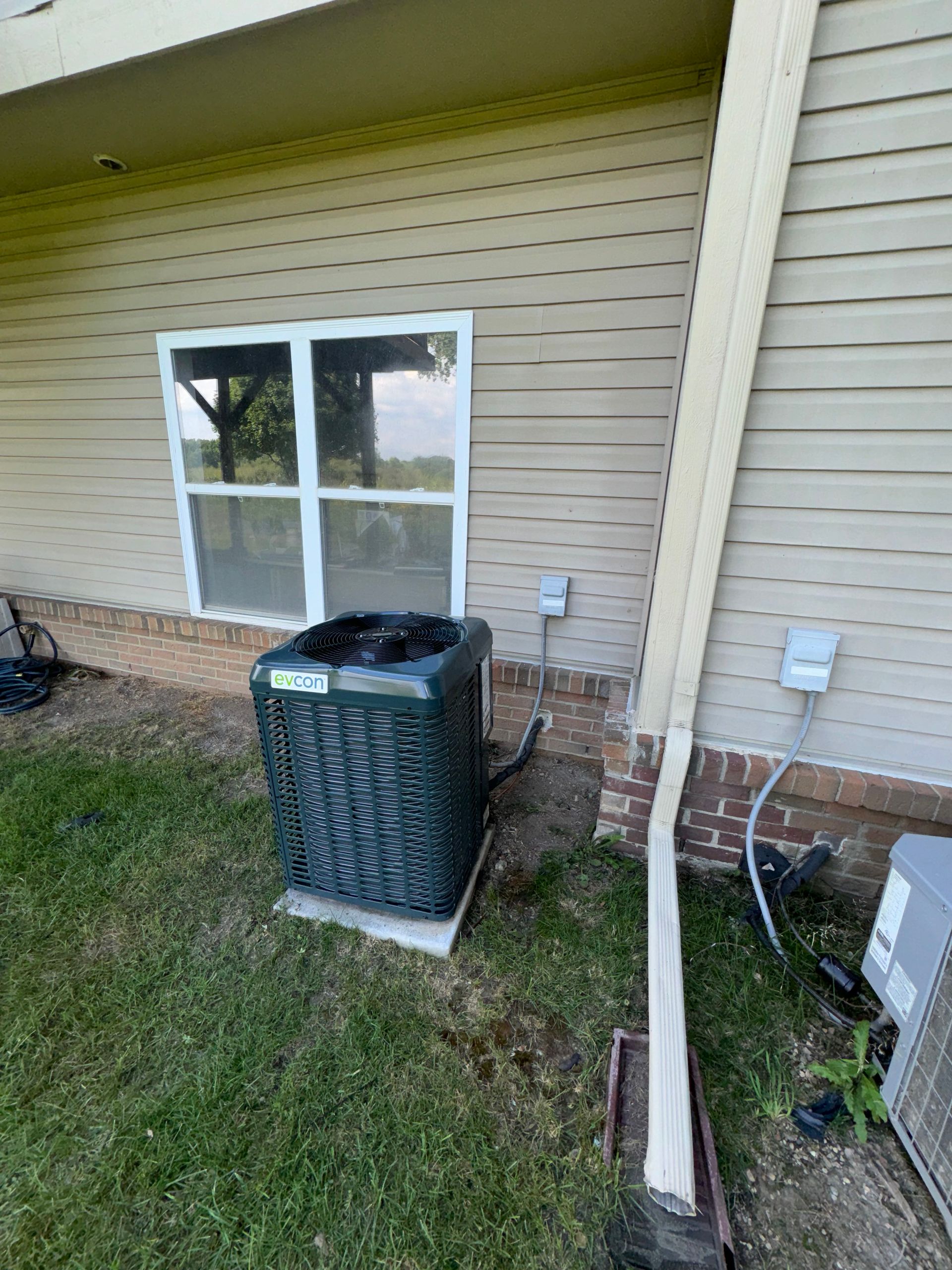 An air conditioner is sitting on the side of a house next to a window.