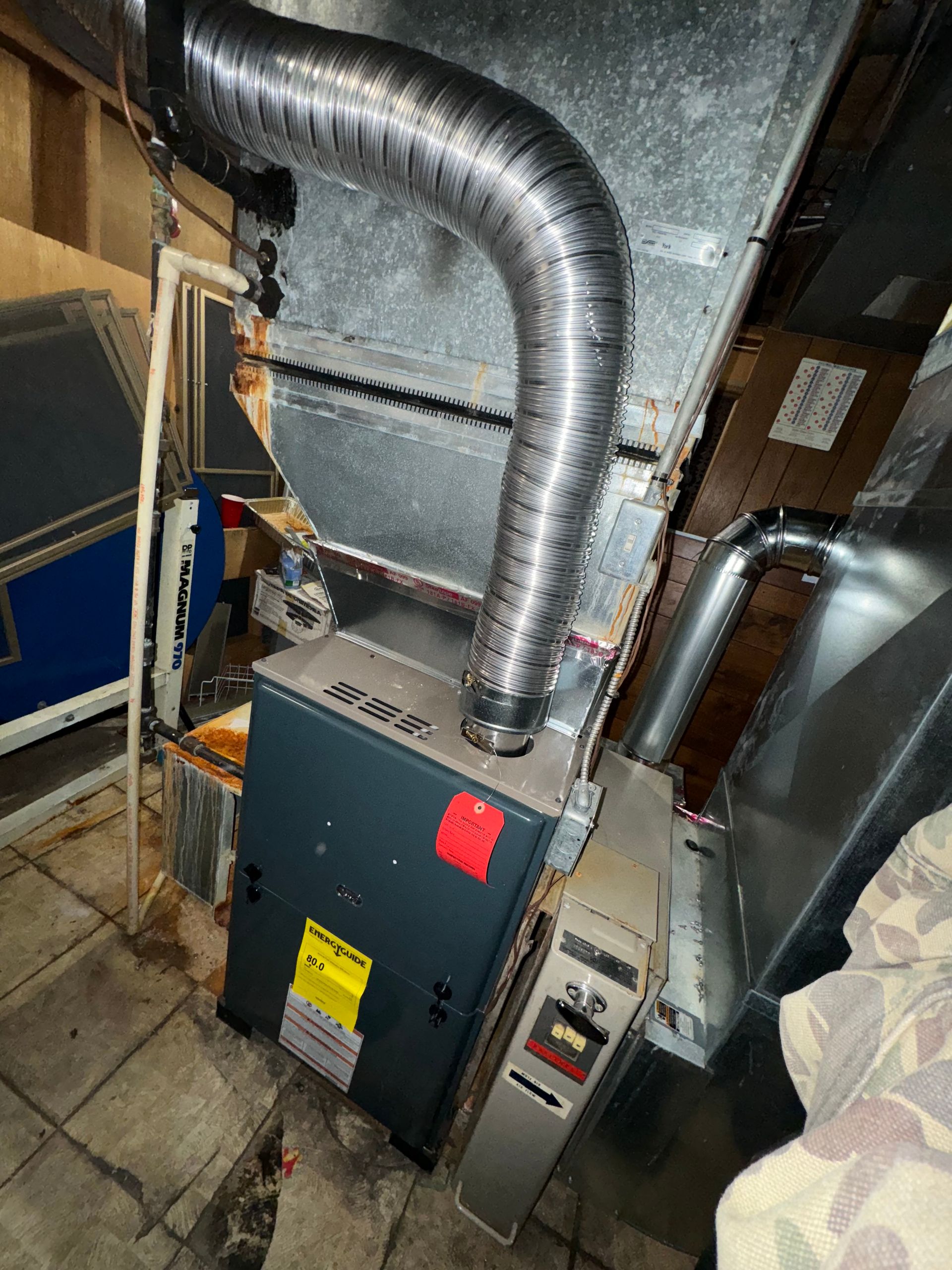 A heater is sitting in the corner of a room next to a duct.