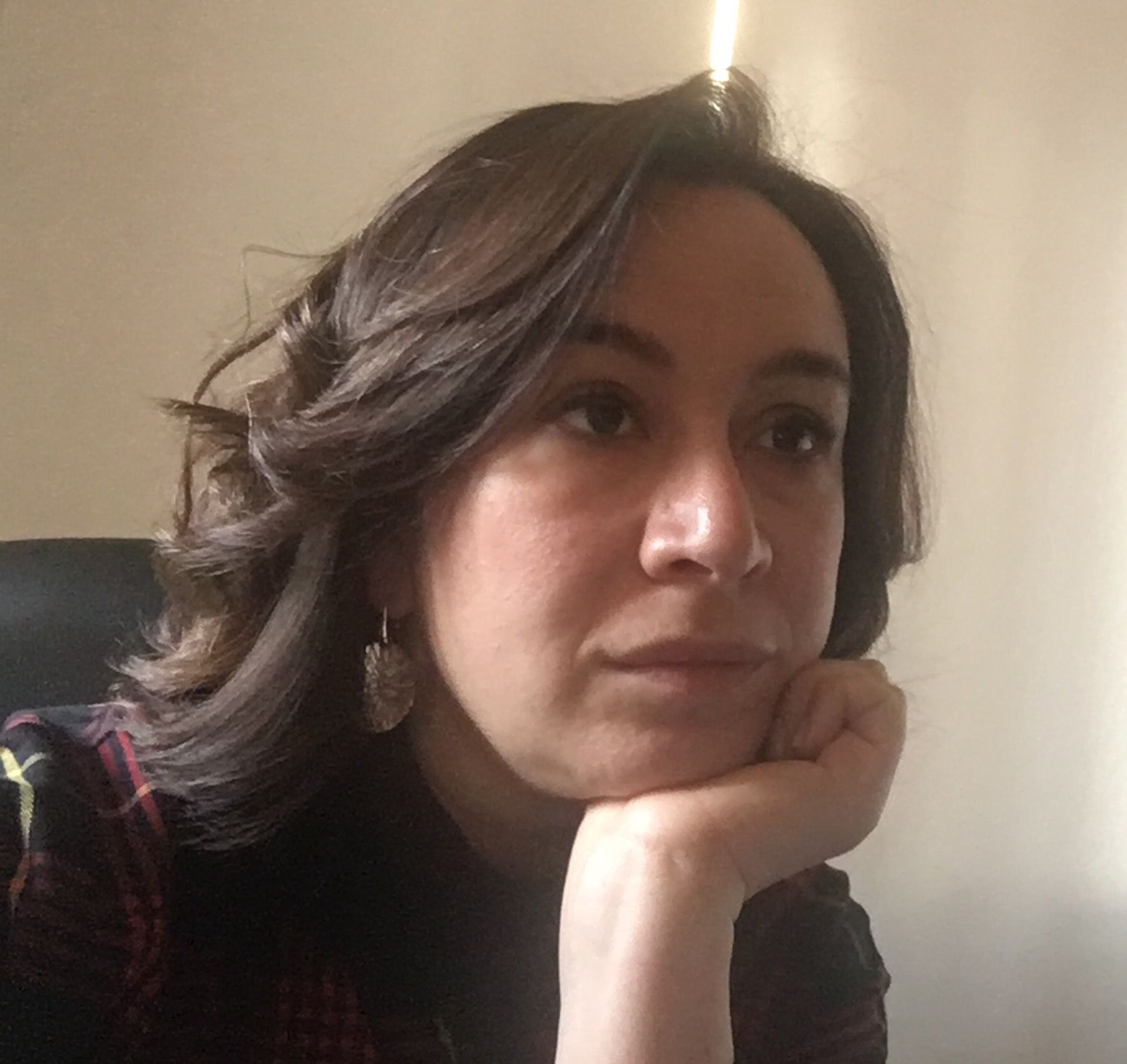 Donna con capelli scuri e ondulati, mento appoggiato sulla mano, sguardo pensieroso.