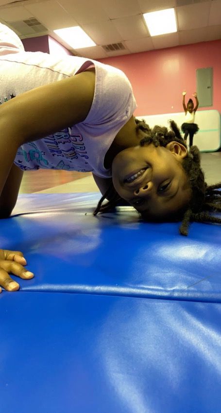 A little girl is doing a handstand on a blue mat.