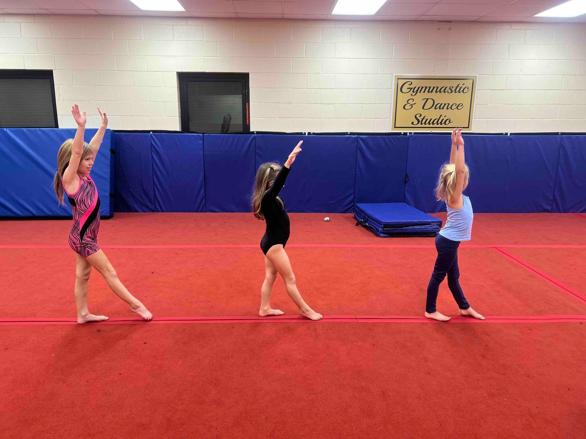 Three young girls are practicing gymnastics in a gym.