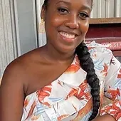 A woman with a braid is wearing a one shoulder top and smiling.