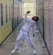 A man in a white tracksuit is standing in a hallway next to a brick wall.